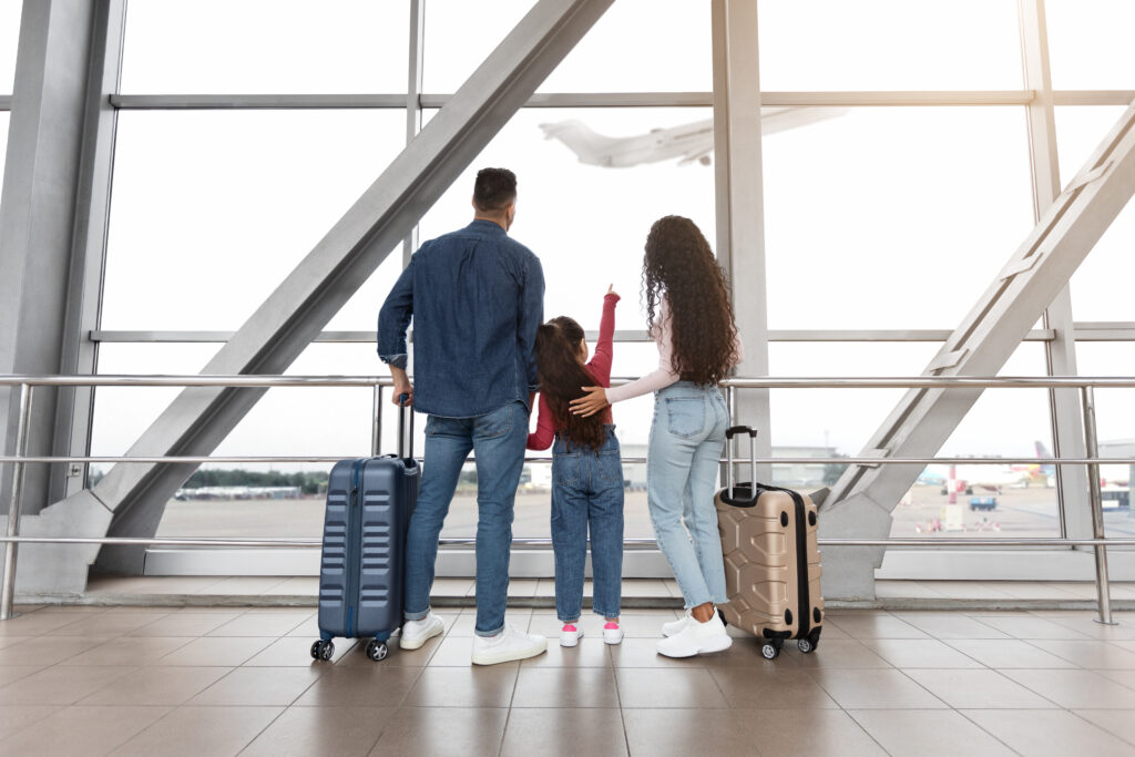 little girl standing with parents in airport, looking at plane out of window